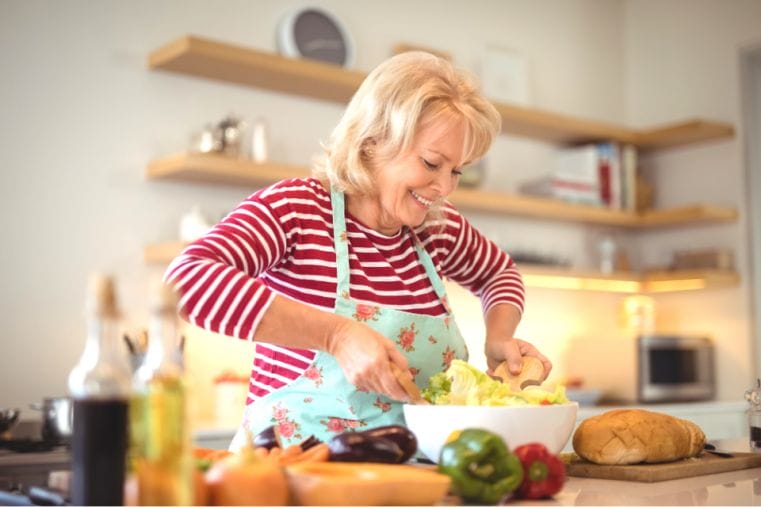 senior woman mixing vegetable salad in kitchen