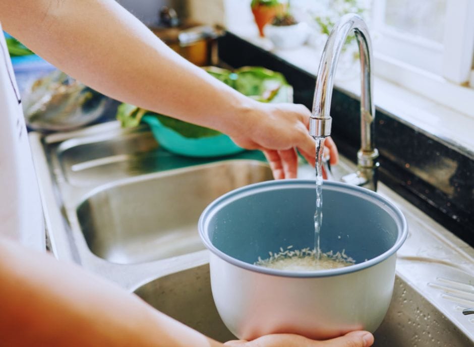 A person pouring water into a bowl in a kitchen sink.