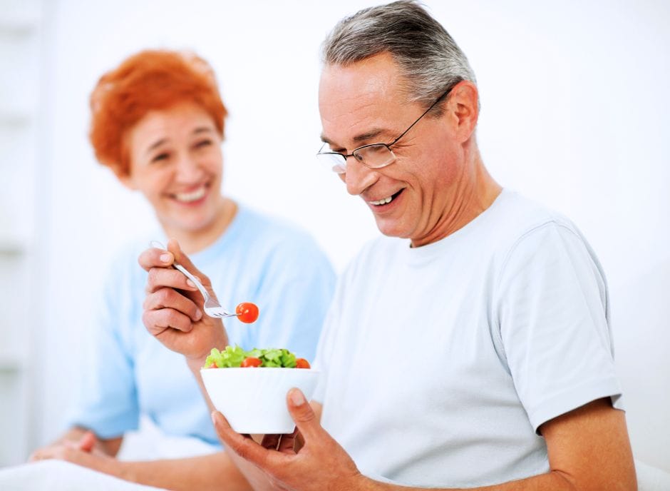 A man and woman eating a bowl of salad.