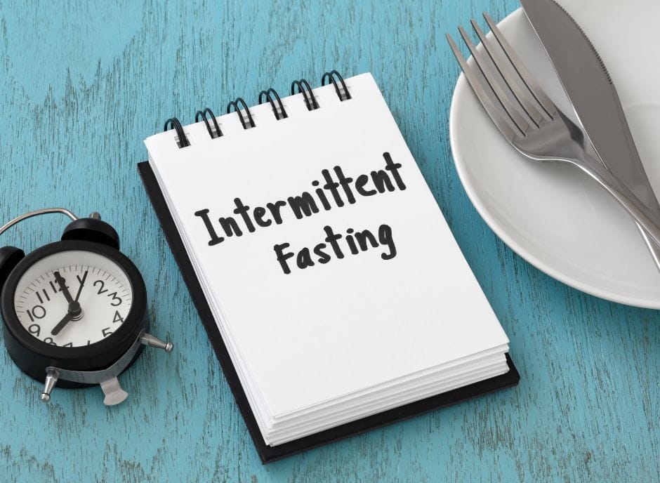 A notepad with the word intermittent fasting next to a fork and knife.