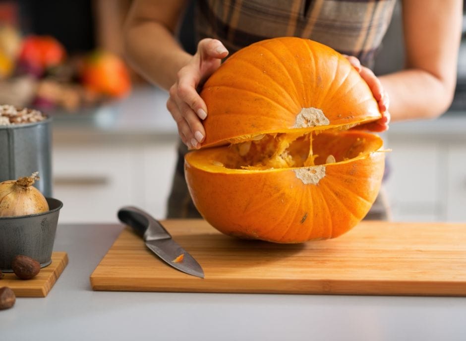 A woman cutting a pumpkin in half on a cutting board.