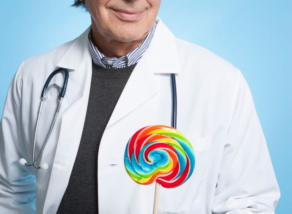 A man in a white coat holding a colorful lollipop.