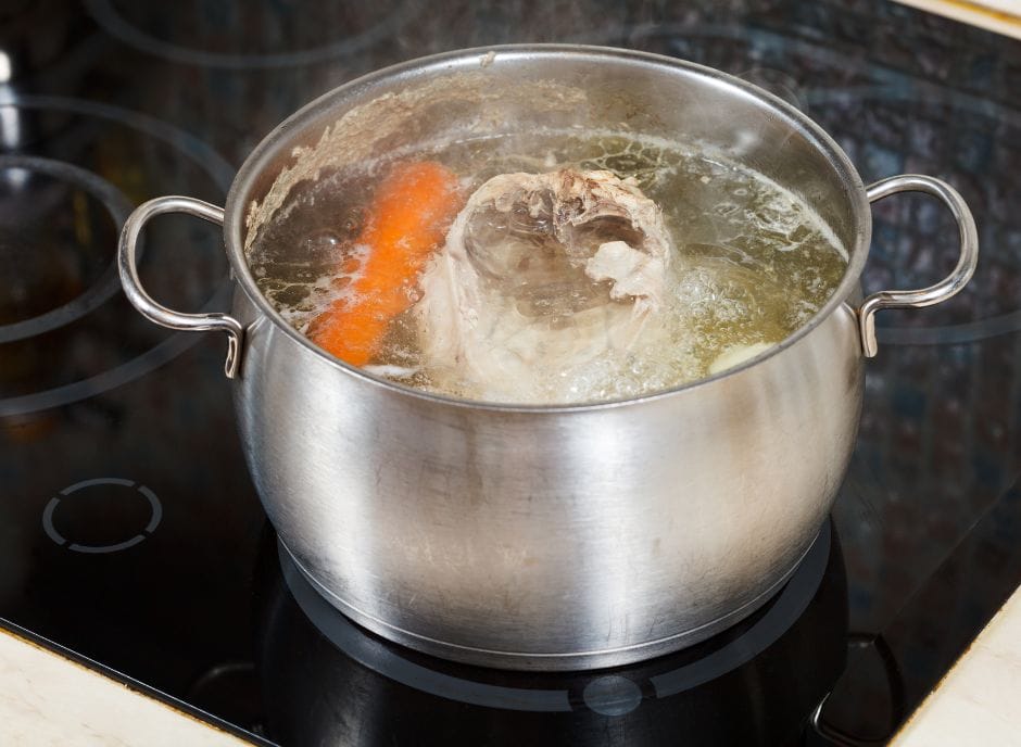 A pot of soup with meat and carrots on the stove.