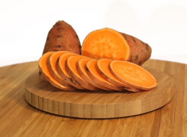 Sliced sweet potatoes on a wooden cutting board.