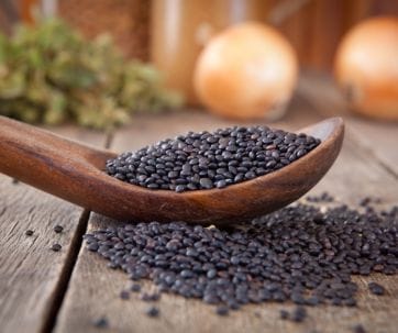 Black sesame seeds in a wooden spoon on a wooden table.