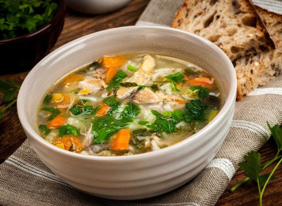 A bowl of chicken soup with vegetables and bread.