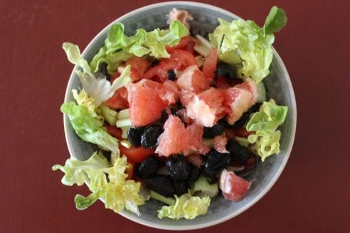 A bowl of salad with grapefruit, black olives and lettuce.
