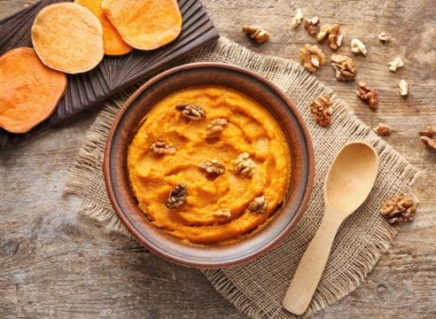 Sweet potato hummus with walnuts in a bowl on a wooden table.