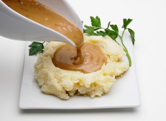Gravy being poured over mashed potatoes.