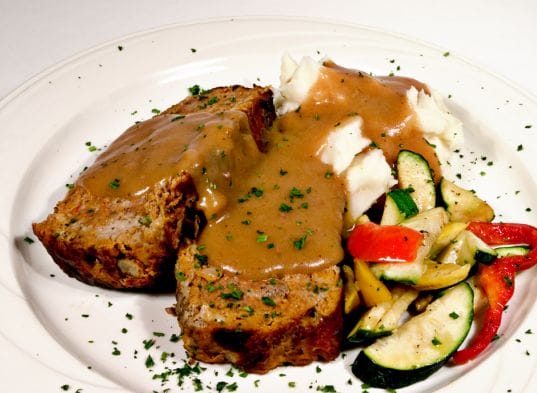 Meatloaf with gravy and vegetables on a white plate.