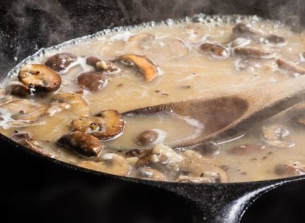 Mushroom soup in a skillet with a wooden spoon.