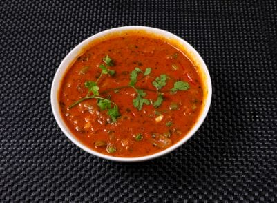 A bowl of red sauce on a black table.