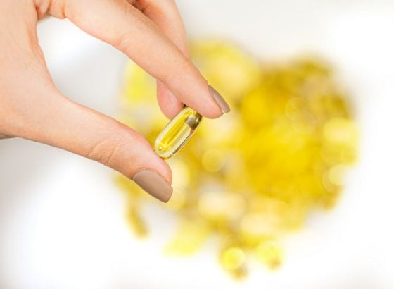 A woman's hand holding a yellow fish oil capsule.