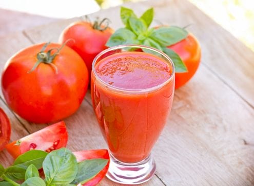 A glass of tomato juice next to sweet potatoes and basil.