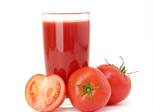 A glass of tomato juice next to a slice of tomato.
