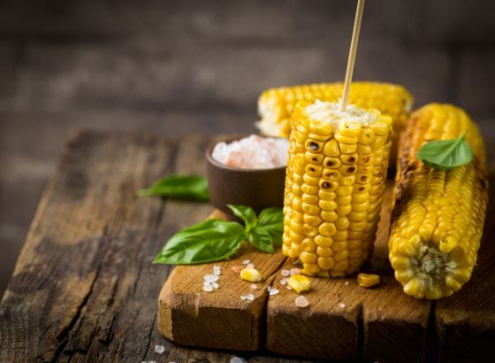 Corn on the cob seasoned with salt and basil, displayed on a rustic wooden cutting board.