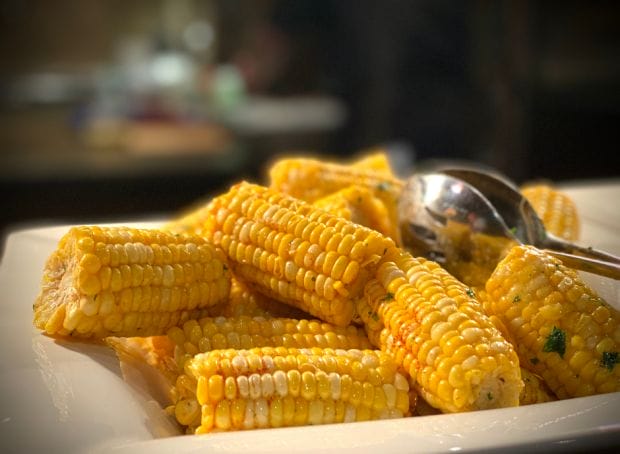 A plate of corn on the cob with a spoon.