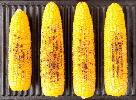 Grilled corn on the cob on a grill with tomato juice glaze.