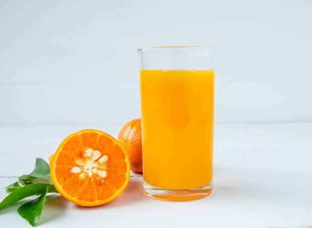 A glass of orange juice next to a slice of orange.