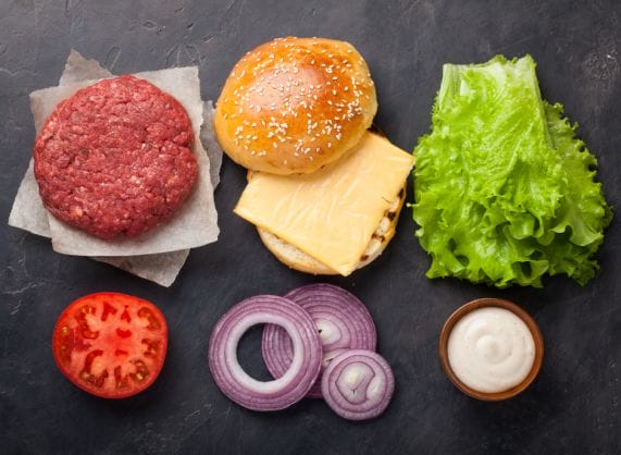 Burgers, tomatoes, onions, lettuce, and mustard on a black background.