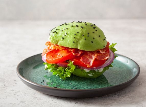 Avocado burger with bacon and tomatoes on a plate.