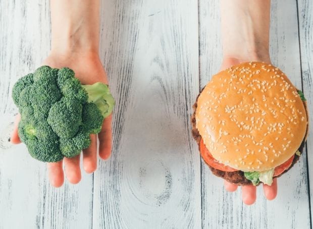 Two hands holding a burger and broccoli.