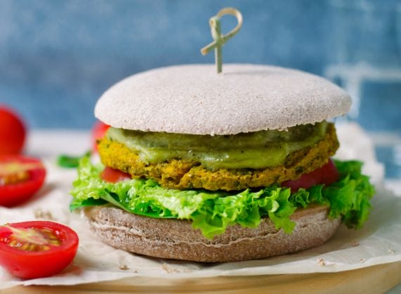 A veggie burger with tomatoes and lettuce on a wooden board.