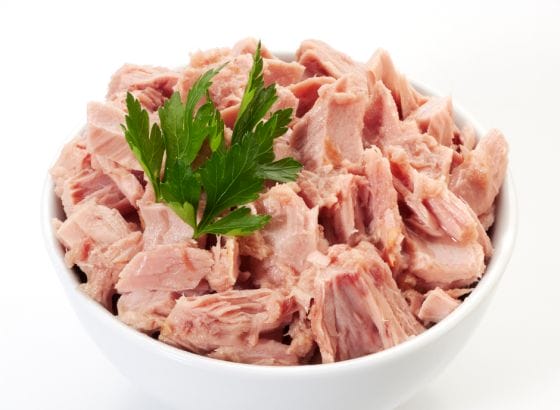 A bowl of tuna with parsley on a white background.