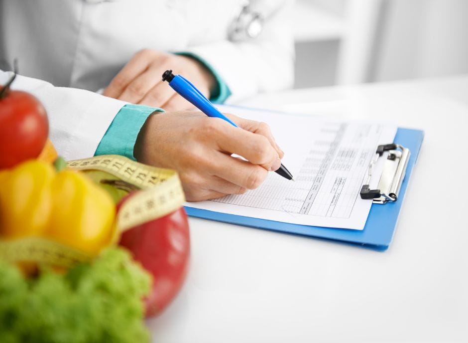 A doctor writing on a clipboard in front of vegetables.