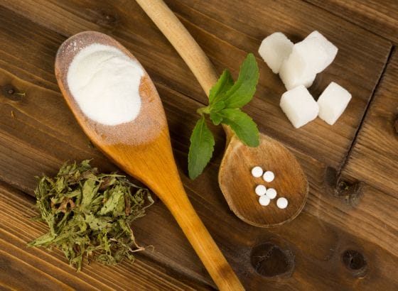 A spoon with sugar and mint on a wooden table.