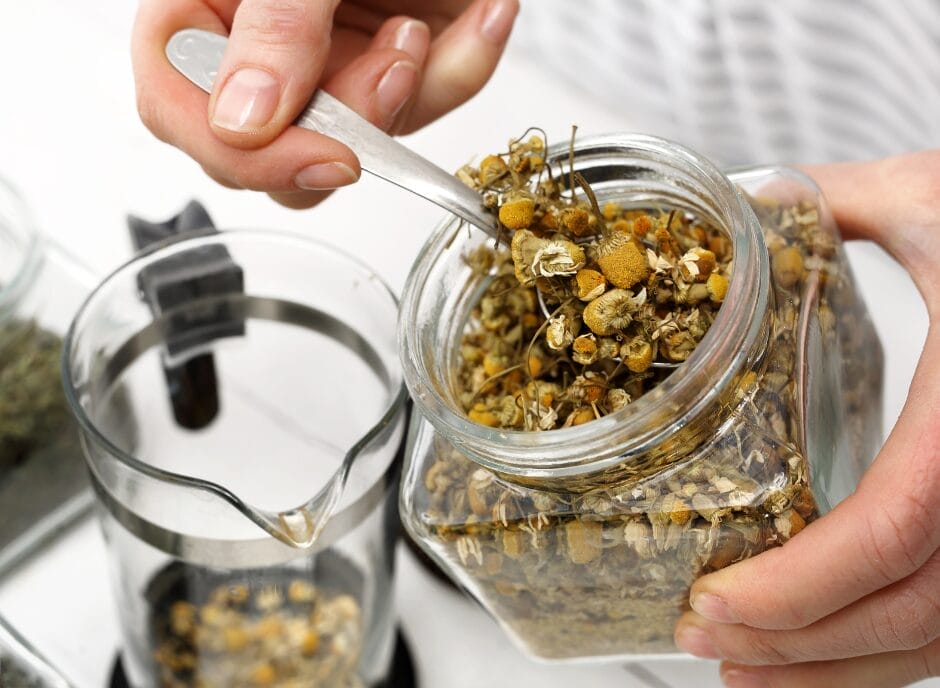 Scooping herbal tea blend from a jar into a tea infuser.
