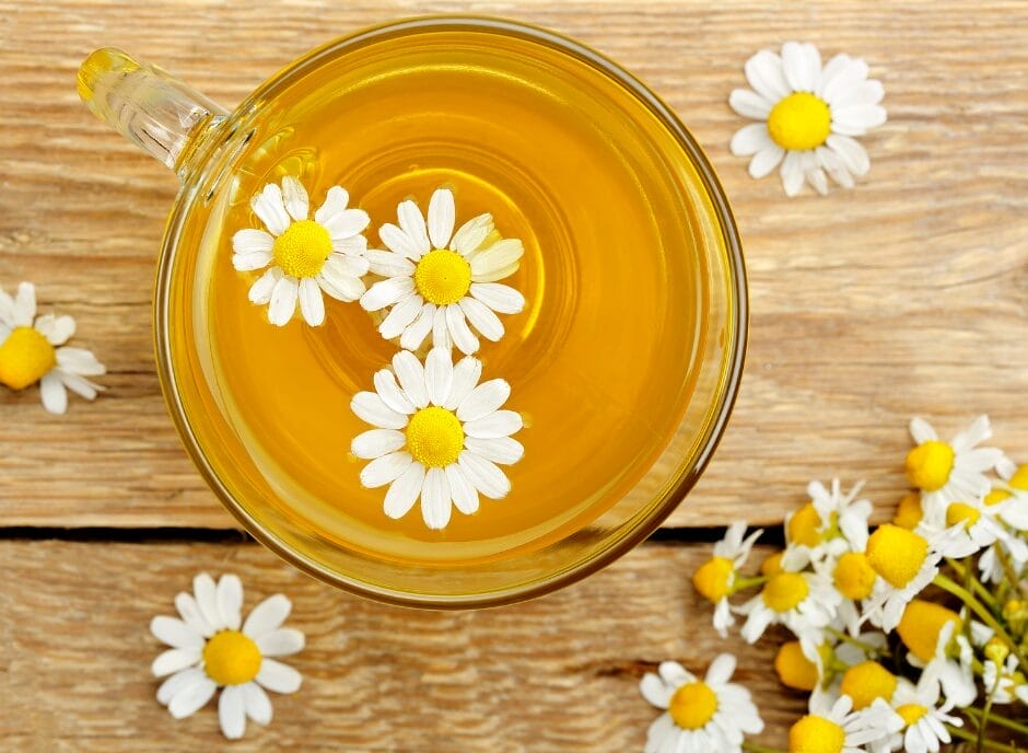 Glass cup of chamomile tea with fresh flowers on a wooden surface.