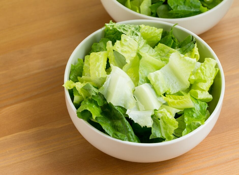 A fresh bowl of chopped green lettuce on a wooden table.