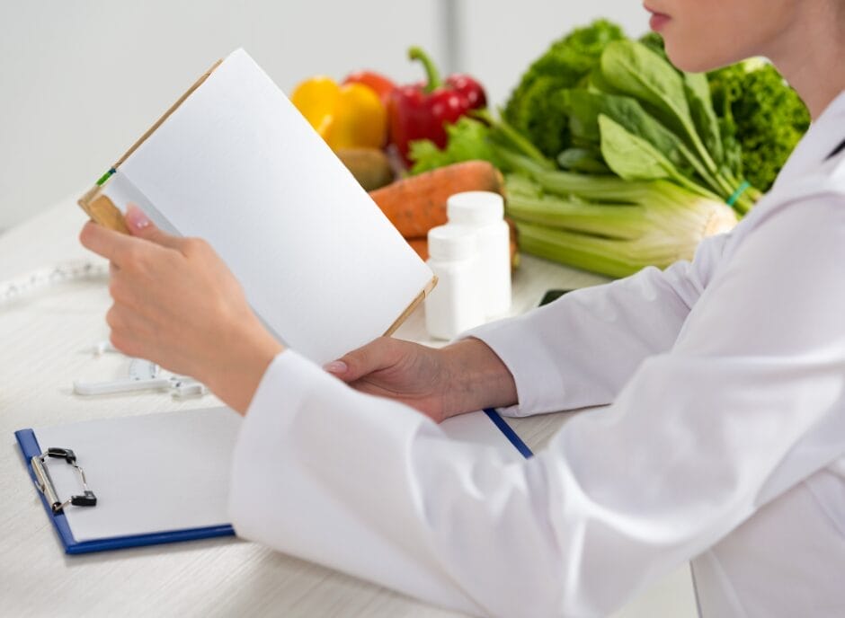 A renal dietitian reviews notes in a clipboard, with fresh vegetables and medical equipment on a table in front of her.